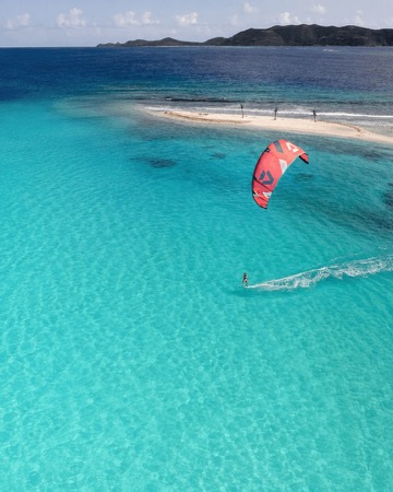 Kitesurfer riding a foil board beneath a red kite over turquoise water